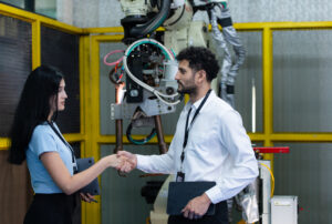 Business partner shaking hands while inspecting on industrial ma